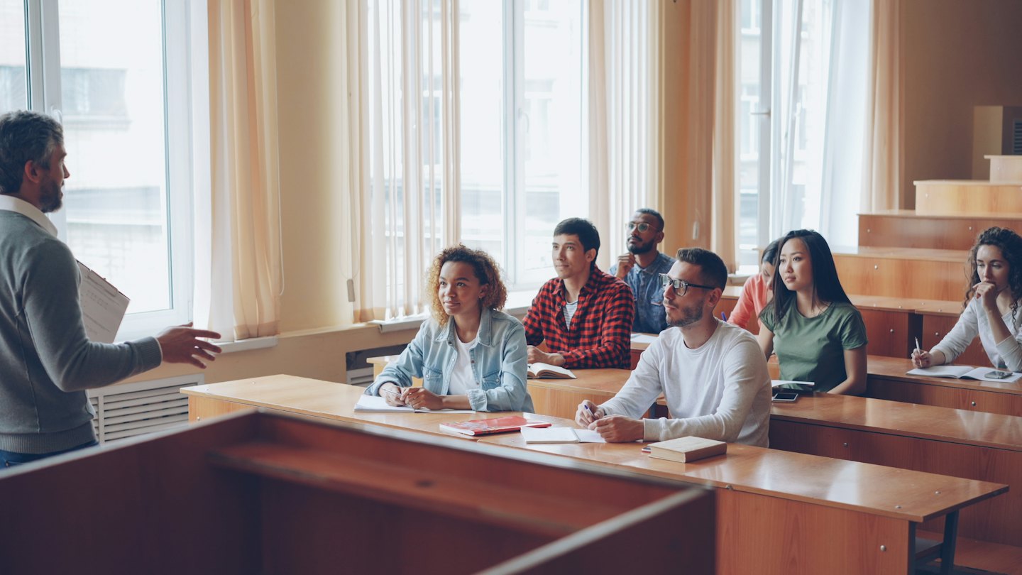 Dozent unterrichtet diverse junge Erwachsene in einem hellen Klassenzimmer.
